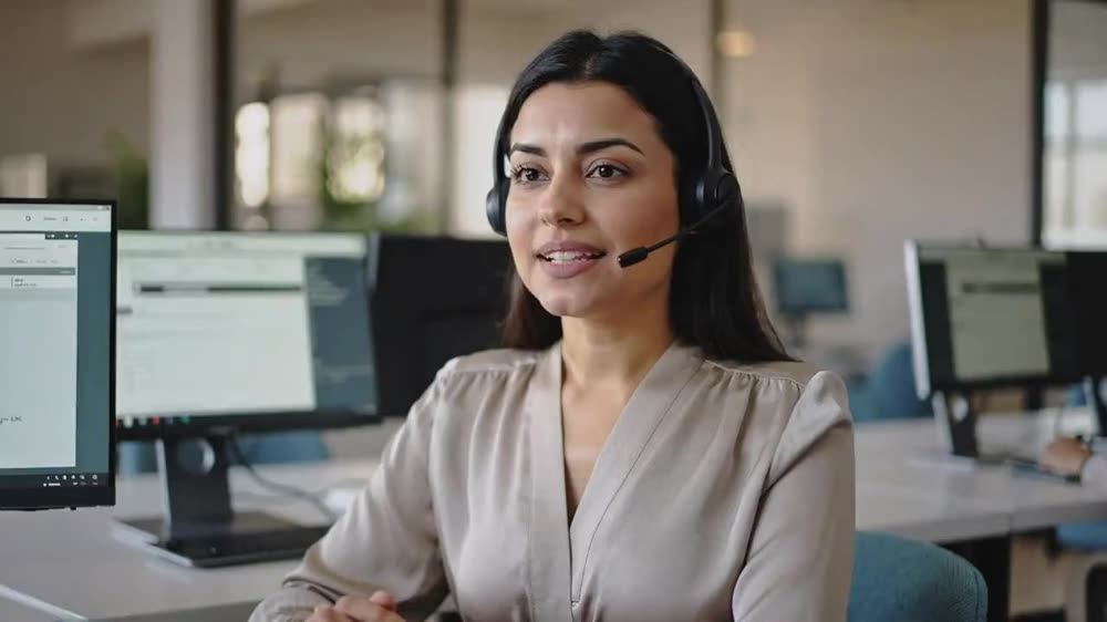 A friendly contact-centre agent wearing a headset at a bright desk.