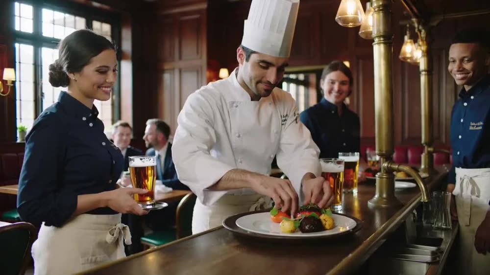 A chef presenting a dish to diners at the bar.
